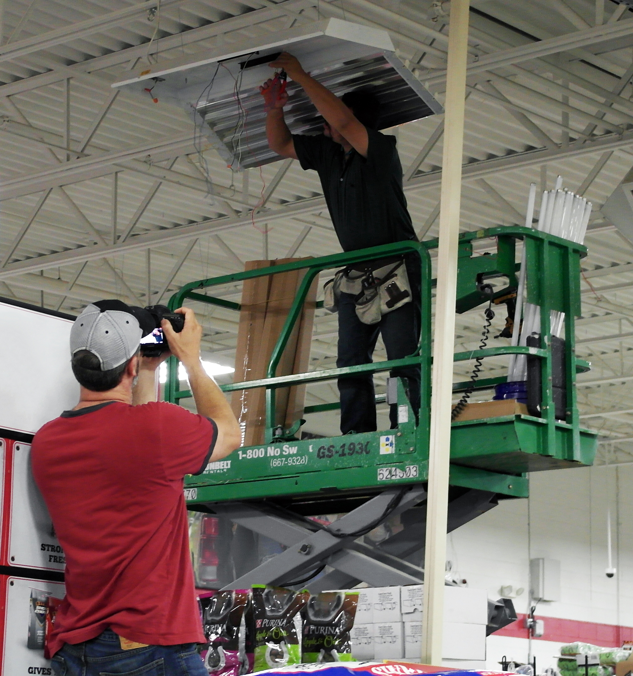EMC photo of a worker standing on a lift, installing a light fixture at a retail location