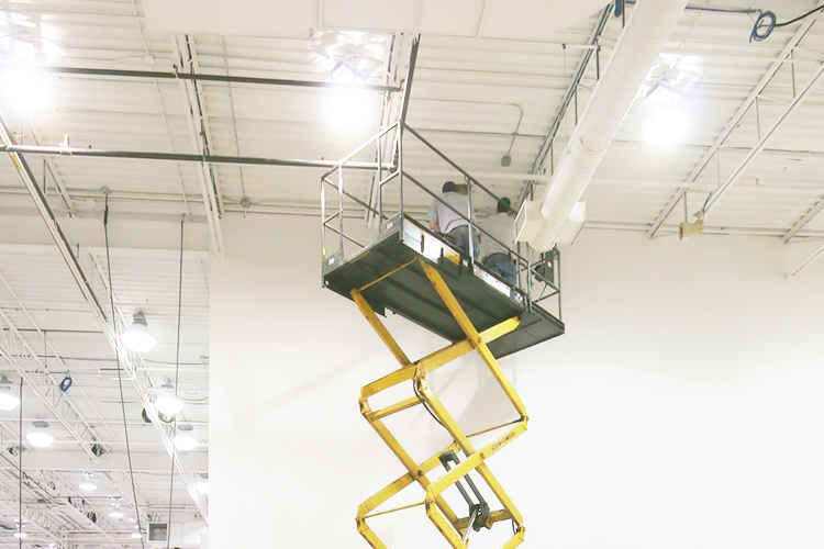 Two men on lift installing highbay light fixtures